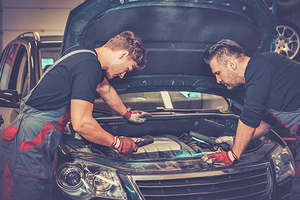 Professional car mechanics checking under hood in auto repair service.