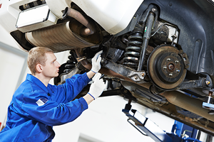 car mechanic inspecting car wheel and suspension detail of lifted automobile at repair service station