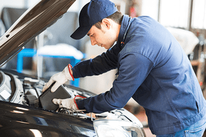 Portrait of an auto mechanic putting oil in a car engine