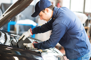 Portrait of an auto mechanic putting oil in a car engine